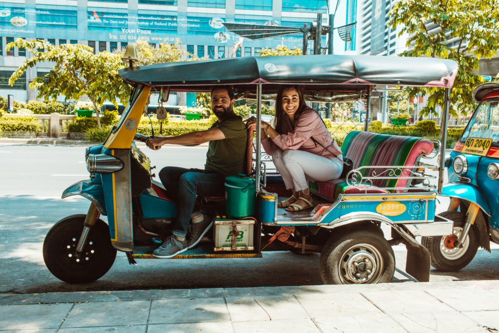 A couple driving and riding as a passenger on a Tuk Tuk in Bangkok